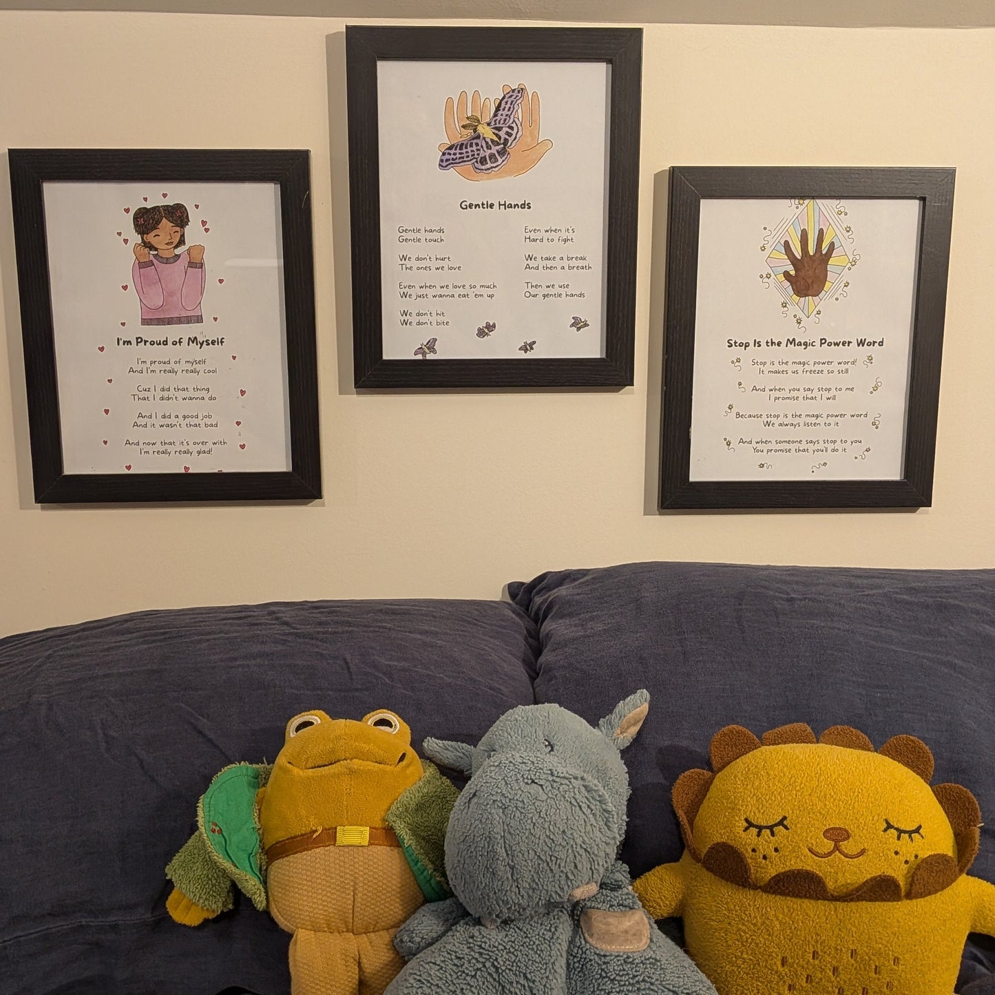 Three stuffed animals (a lion, a elephant, and a monkey) sitting on a couch with framed mama nous song lyric posters behind them.