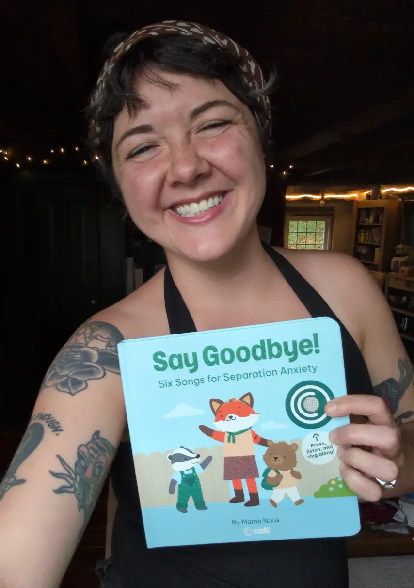 a smiling mama nous holds a copy of "say goodbye" in a dimly lit room.